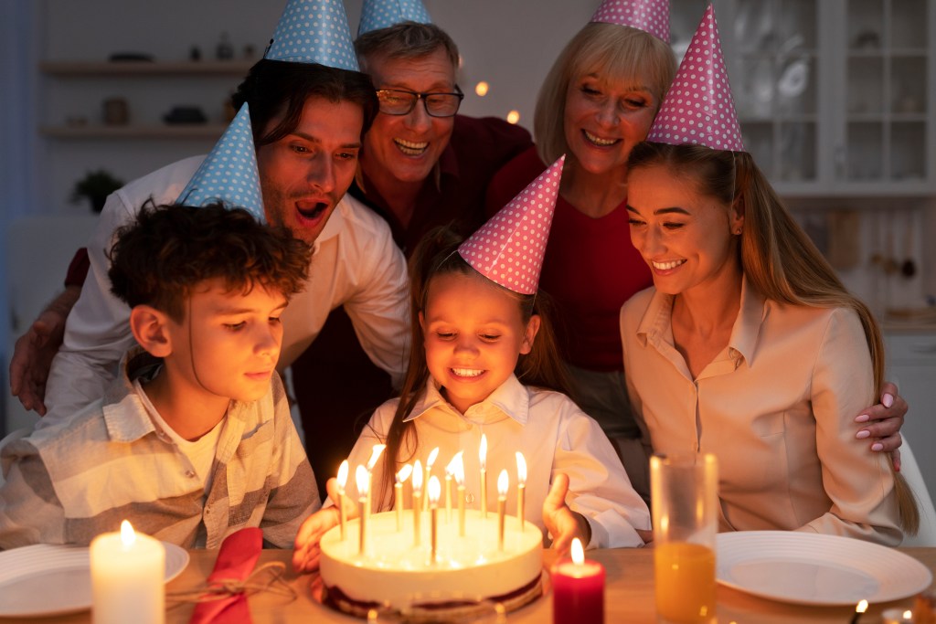 The little girl who was taking a birthday cake with lit candles, celebrating with her extended family at home.