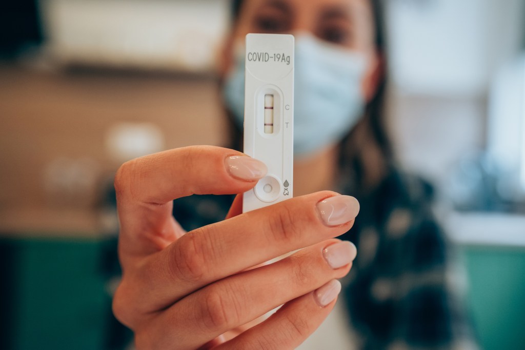 The doctor's hand on protective gloves that holds a positive positive result of Covid-19 test