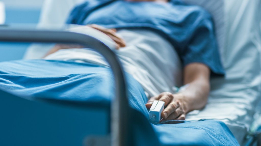 Sick male patient sleeping on a hospital bed with a heartbeat monitor attached to his finger