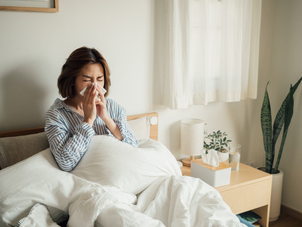 Asian woman suffering from the flu, sneezing in tissues, only in a bedroom