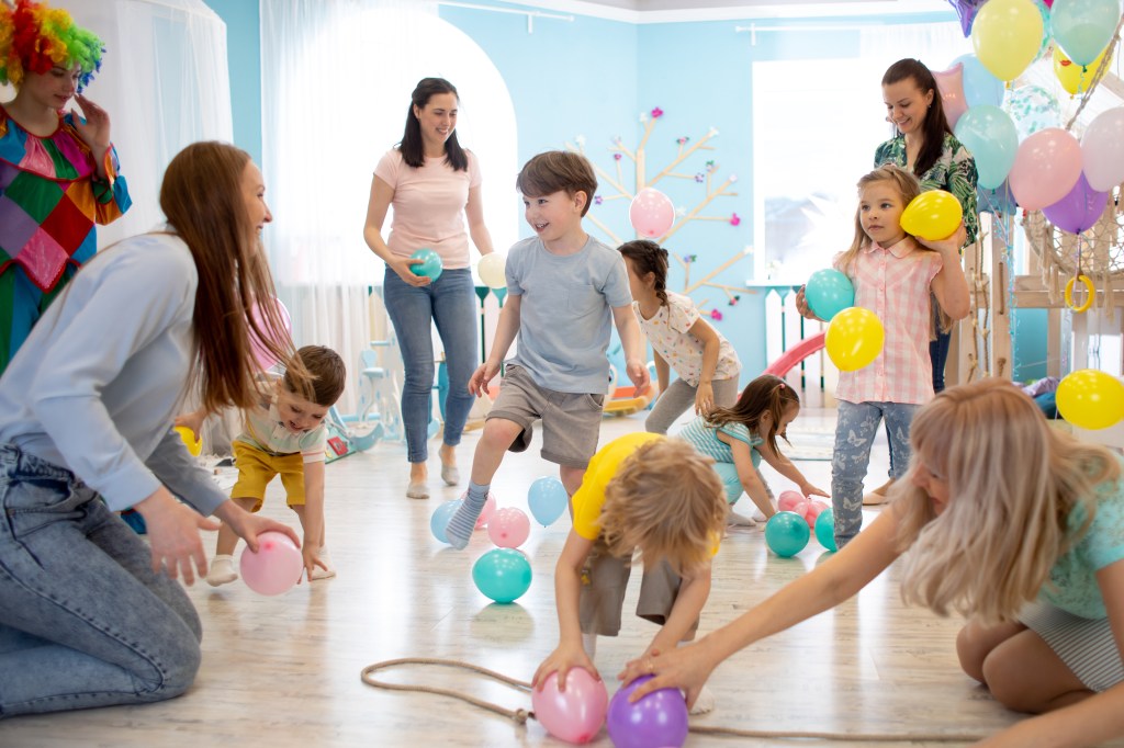 Happy children and their mothers, including Suzi Gardner and Ella Anderson, having fun with colorful balloons at a birthday party