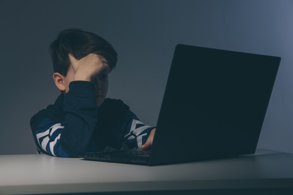 Bored teenage boy using a laptop, experiencing online attack.