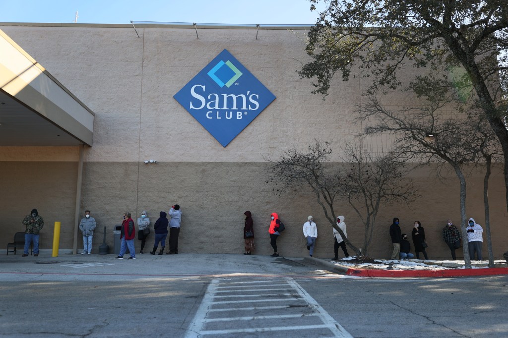 People who wear masks wait in line outside a summit club during a power outage.