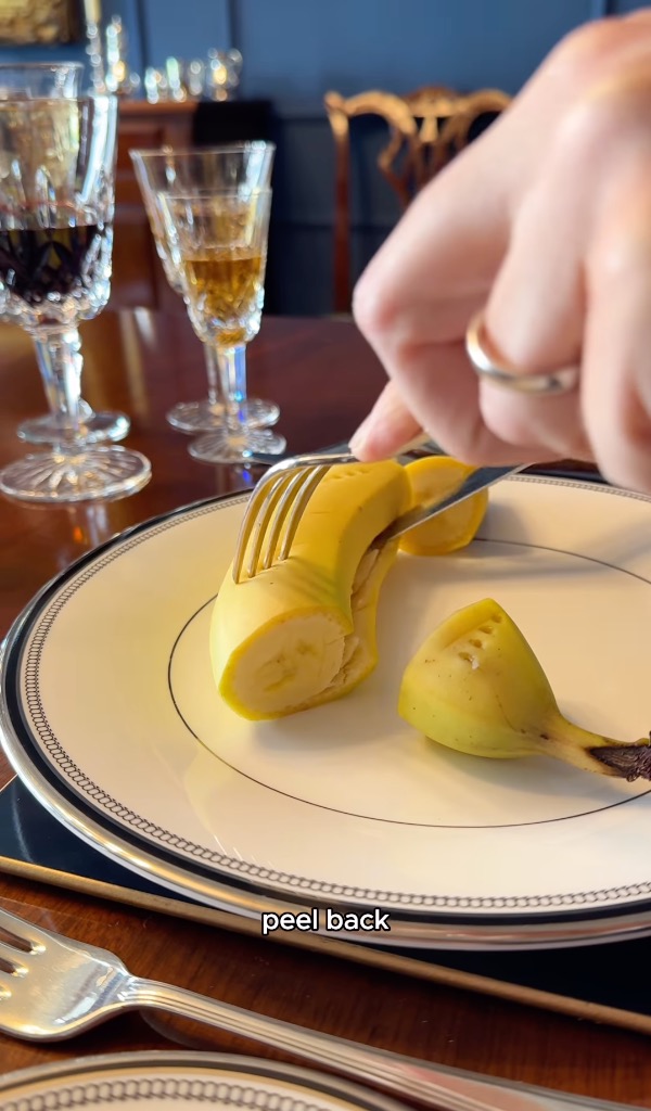 A banana being cut with a fork and knife on a plate.